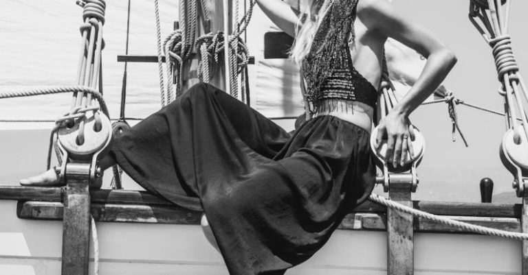 Hull - Black and white full body side view of stylish female in hat sitting on wooden ship during cruise on summer day