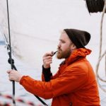 Boat - Man in Orange Jacket Holding a Tabaco Pipe While Sitting on the Boat