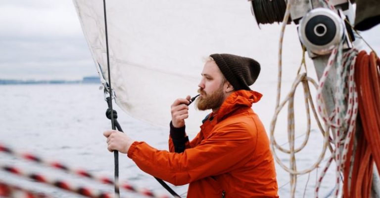 Boat - Man in Orange Jacket Holding a Tabaco Pipe While Sitting on the Boat